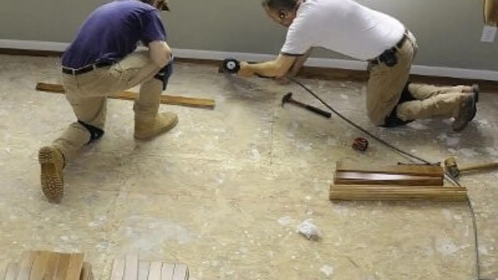 Two workers kneeling on a bare subfloor while installing new flooring